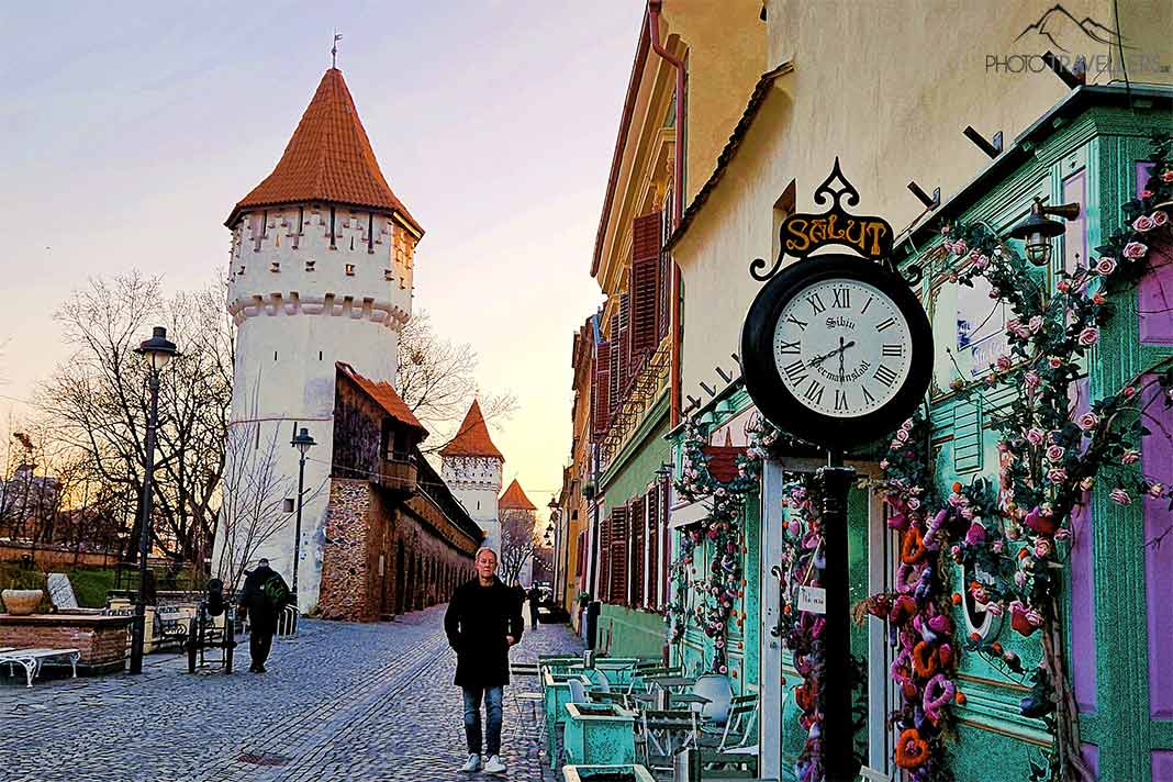 Ein Mann läuft auf der Zitadellenstraße vor drei weißen Wehrtürmen mit orangefarbenen Ziegeln und bunten Fassaden von Lokalen gegenüber