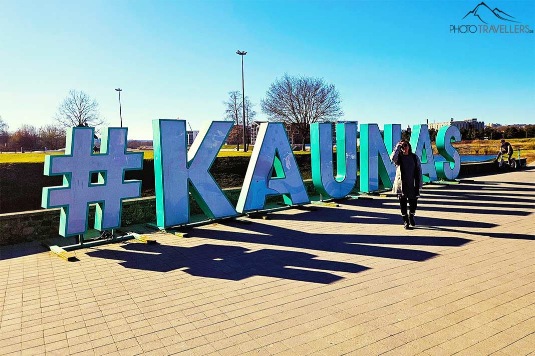 Eine Frau steht vor einem türkisen Schriftzug mit Kaunas