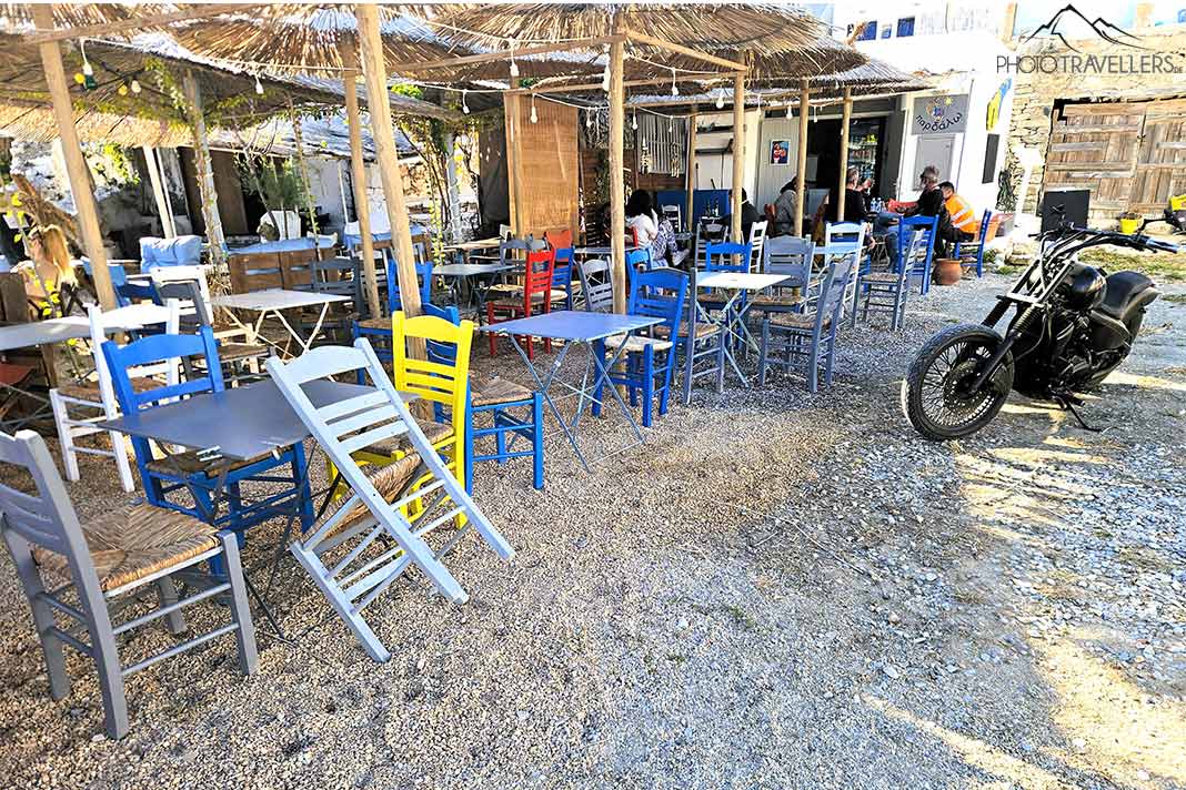Bunte Stühle einer Beachbar und ein schweres Motorrad mit einigen Gästen daneben