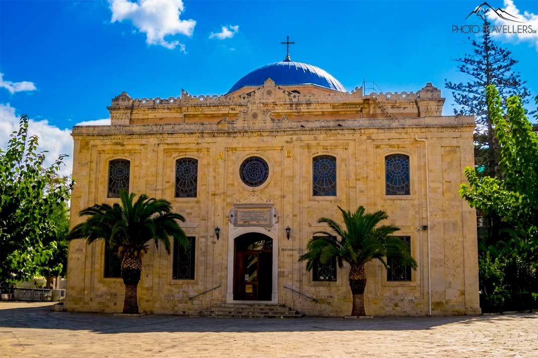 Vor der steinernen Kirche Agios Titos mit der blauen Kuppel stehen zwei Palmen