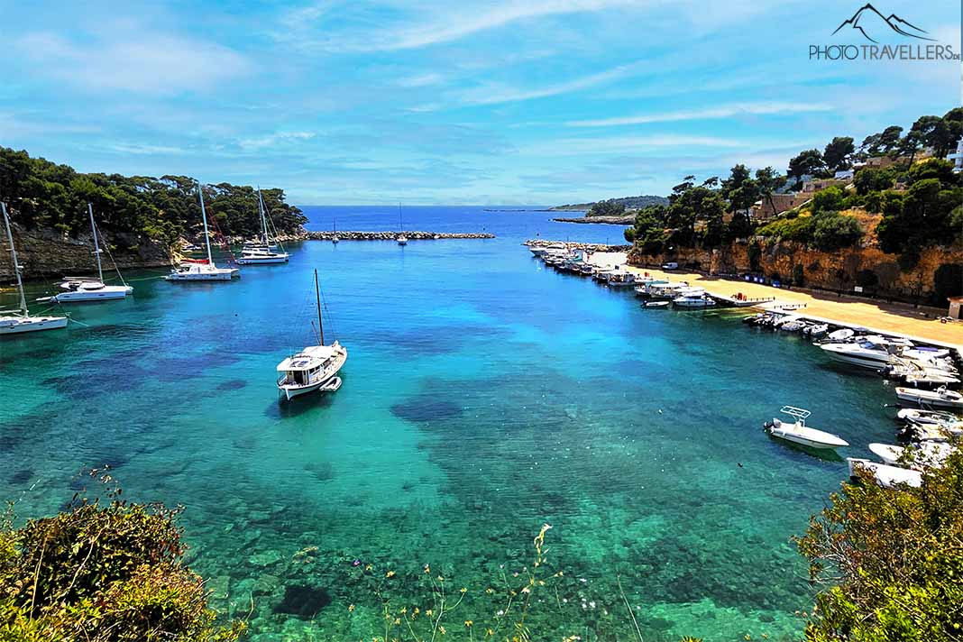 Ein Segelboot ankert in der türkisschimmernden Bucht von Votsi mit Bäumen entlang des Ufers