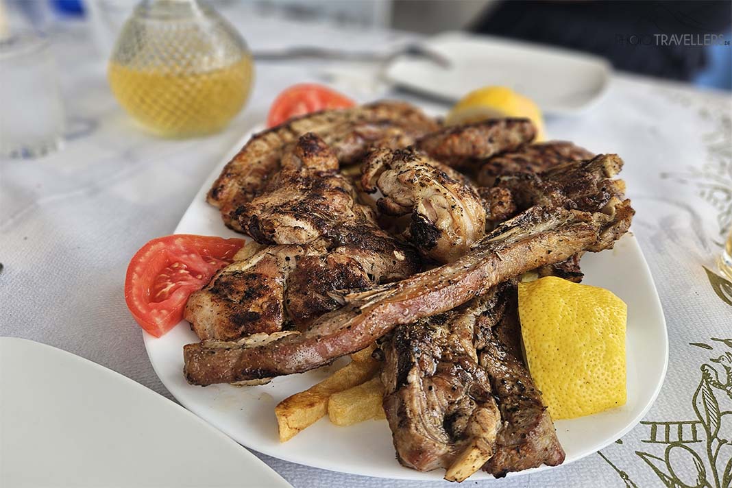 Eine Grillplatte mit Schwein, Lamm und Huhn auf einem Teller angerichtet mit Zitronen und Tomaten