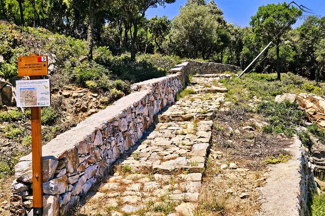 Eine kleine Wandertafel am Rande eines gepflasterten Steinpfads am Berg  Palouki 