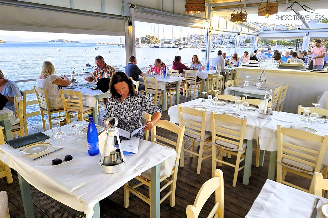 Menschen sitzen an den gedeckten Tischen der Meerterrasse der Taverne Bakaliki