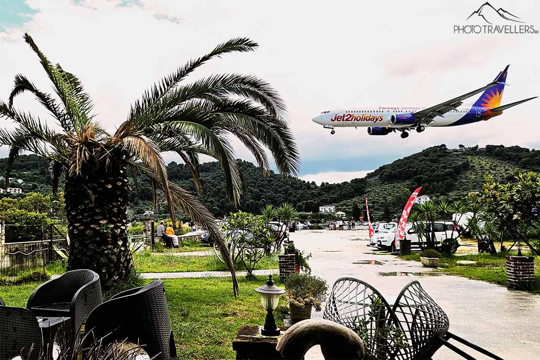 Blick vom Cafe mit Palmen auf ein landendes Flugzeug in Skiathos