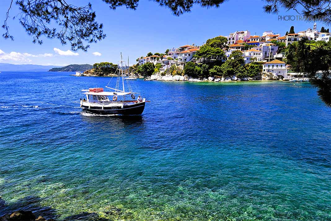 Ein Ausflugsboot vor dem türkisfarbenem Meer mit Häusern und Bäumen in Skiathos