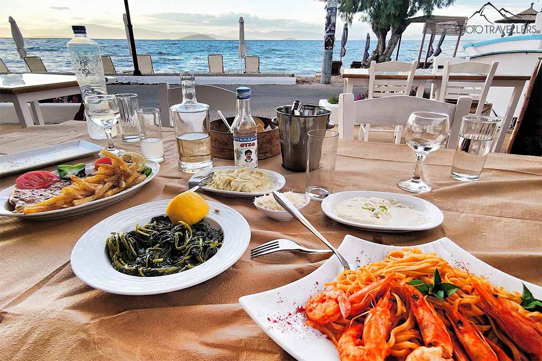 Drei Teller mit Shrimps, Chorta und Beilagen stehen auf dem Tisch einer Strandtaverne