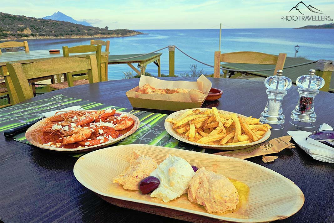 Vier Teller auf dem Tisch einer Taverne am Meer mit Shrimps in Tomatensauce, Tzatziki und Pommes und