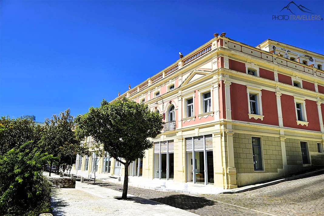 Das zweistöckige Archäologische Museum im neoklassizistischen Stil in braun und gelb hinter mehreren Bäumen
