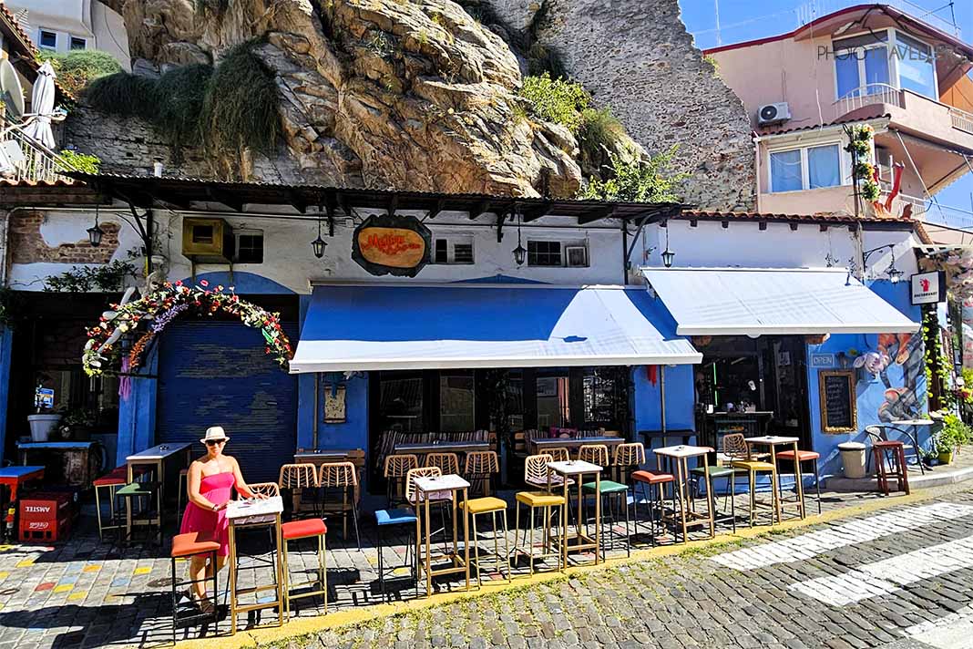 Eine Frau im pinkfarbenen Kleid lehnt an einem Stehtisch eines blau-bemalten Cafés