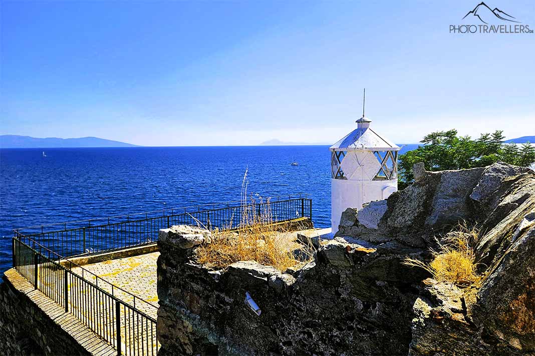 Leuchtturm von Kavala auf einer umzäunten Plattform mit Felsen und Büschen dahinter