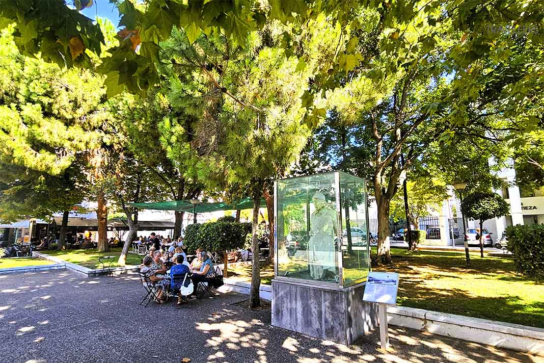 Kleiner Park unter großen Platanen mit einer Skulptur zwischen den Pflanzen