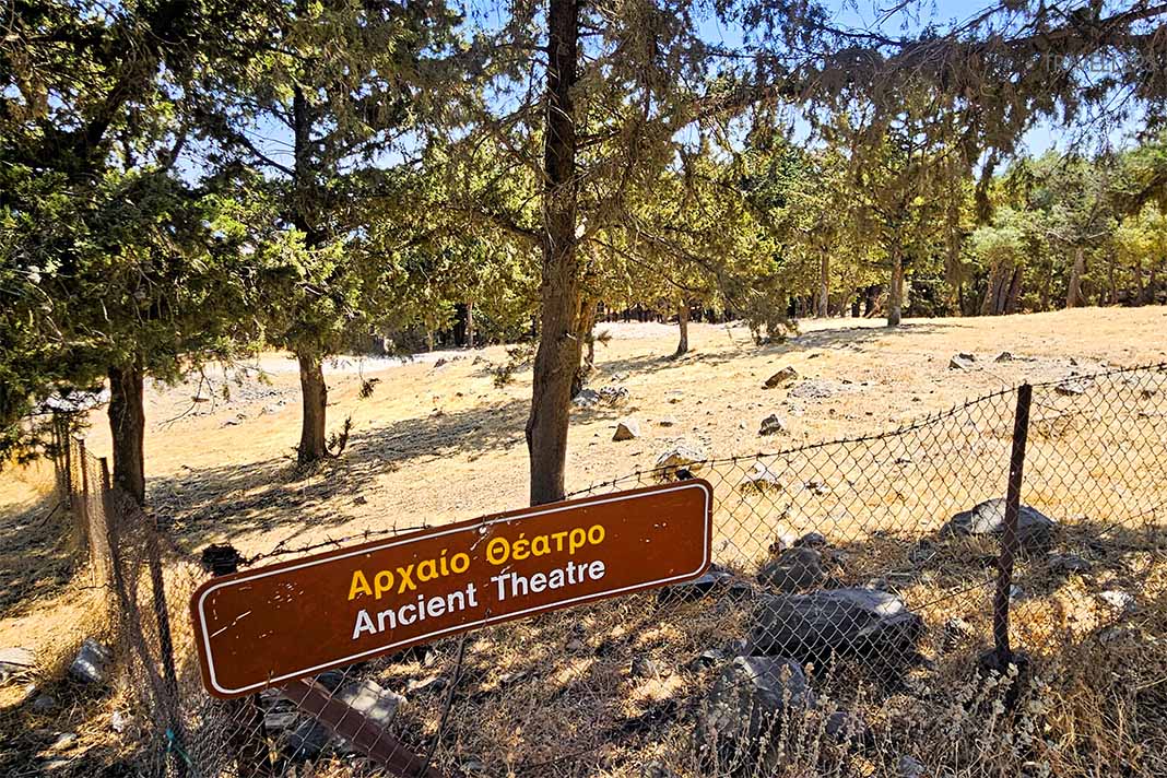 Ein braunes Schild mit der Aufschrift Ancient Theatre in einem Wald mit Nadelbäumen