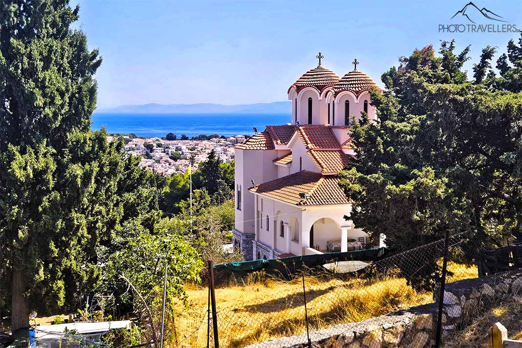 Die zwei Türme der Dreifaltigkeitskirche zwischen Bäumen oberhalb der Häuser von Mytilini