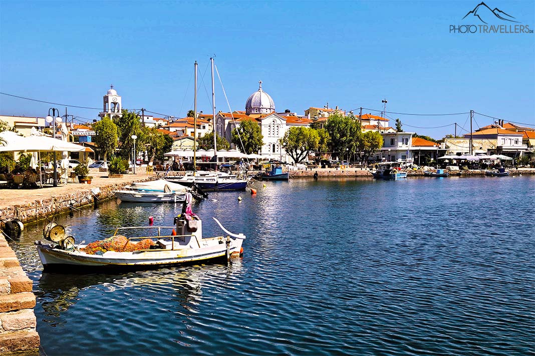 Ein kleines Holzboot ankert im Hafen von Panagoudia mit einer Kuppelkirche und Häusern im Hintergrund