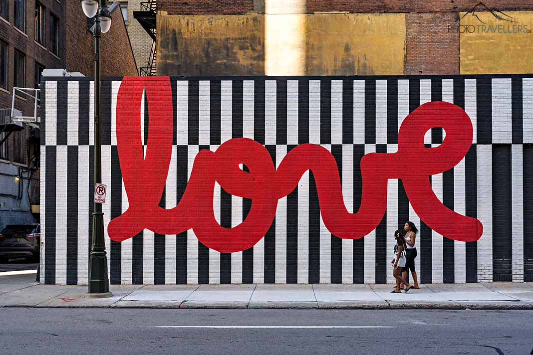 Zwei Frauen laufen an einem riesigen Love-Schriftzug an einer Hauswand vorbei